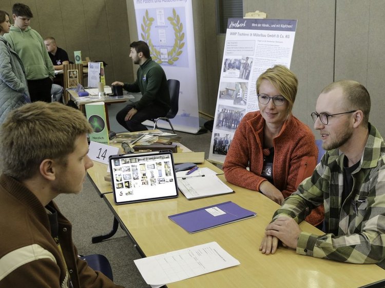 Impressionen der Lehrstellenbörse Zehdenick 2025 Das Foto zeigt den Messestand der Tischlerei Großwoltersdorf - zwei Standbetreuer im internsivern gespräch mit einem Besucher