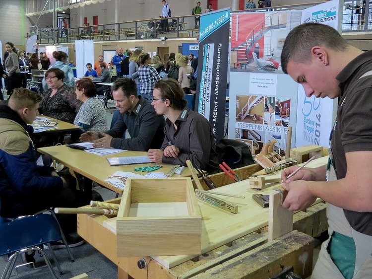 Impressionen von der Lehrstellenbörse 2015 Das Foto zeigt den Messestand der Firma Fritz Müller, drei Personen sind im Gespräch, ein junger Mann bearbeitet Holzteile