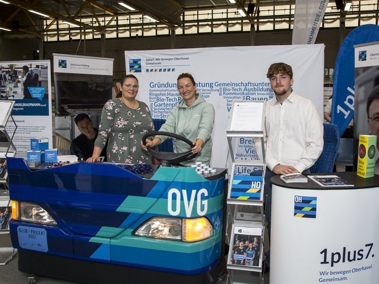 Impressionen der Lehrstellenbörse 2024 Das Foto zeigt die drei Personen am Messestand der OVG, dessenTresen wie ein Bus gestaltet ist