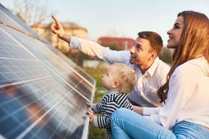 Das Foto zeigt eine junge dreiköpfige Familie vor einem Solarpanel