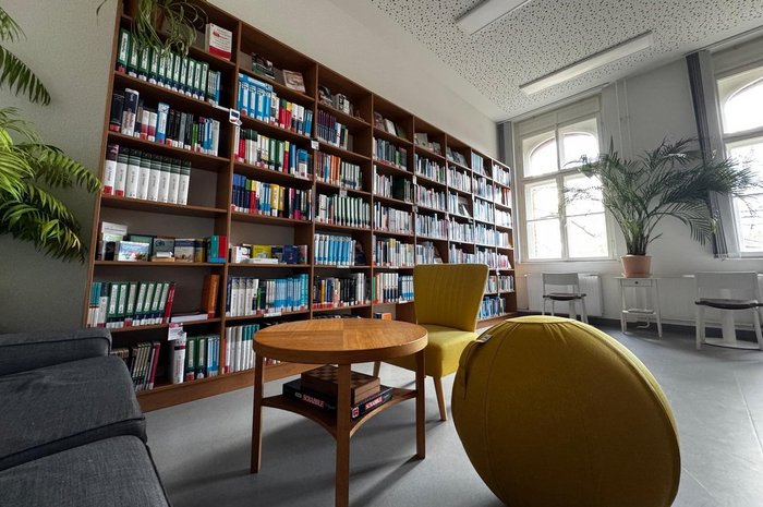Das Foto zeigt einen Raum mit großem Bücjerregal und einer Leseecke