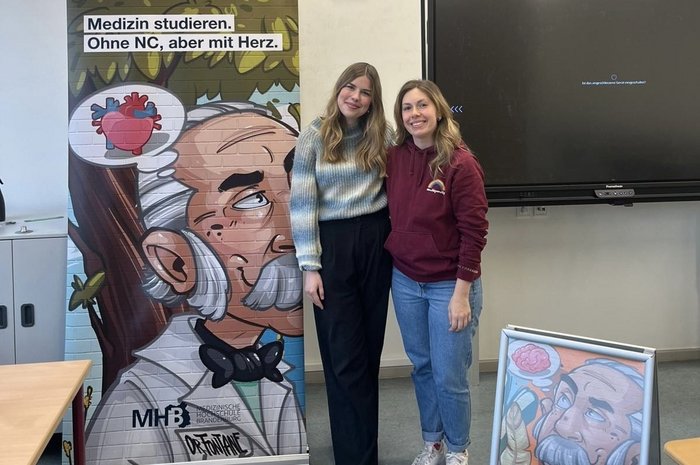 Das Foto zeigt zwei junge Frauen vor einem Roo-up der MHB Neuruppin