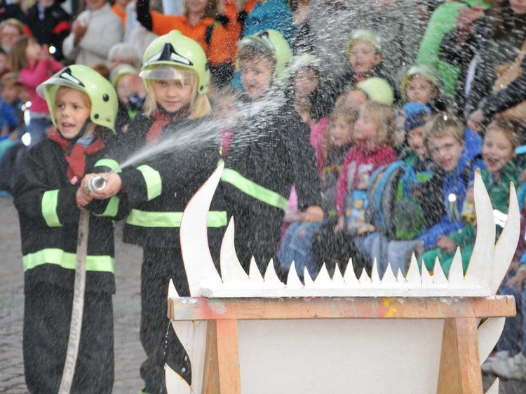 Kinder die der Jungfeuerwehr angehören, halten einen Wasserschlauch in der Hand, im Hintergrund sind weitere Kinder zu sehen.