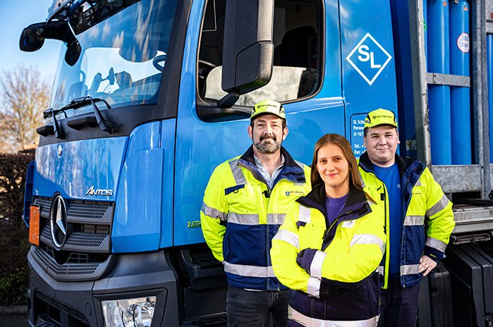 Das Foto zeigt eine Auszubildende mit ihren Mentoren vor einen LKW