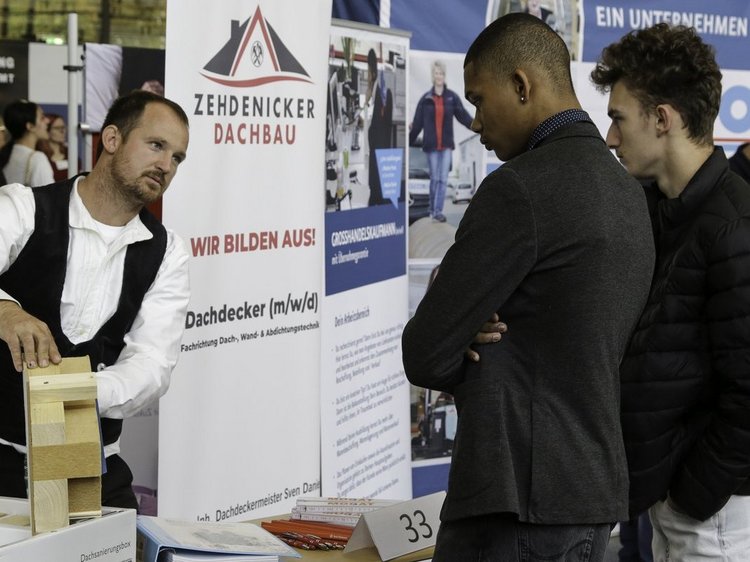 Impressionen der Lehrstellenbörse Zehdenick 2025 Das Foto den Messestand vom Zehdenicker Dachbau - Sven Daniel erklärt zwei jungen Männern ein Holzmodell eines Dachstuhlesines