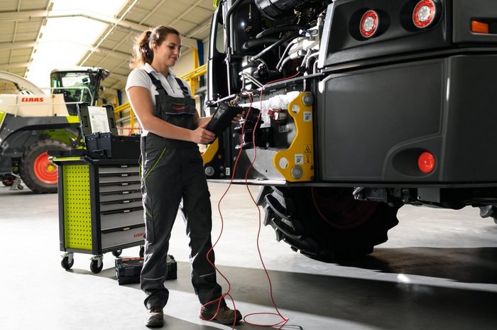 Das Foto zeigtr eine junge Mechatronikerin mit einem elektronischem Prüfgerät an einem Landwirtschaftsfahrzeugs 