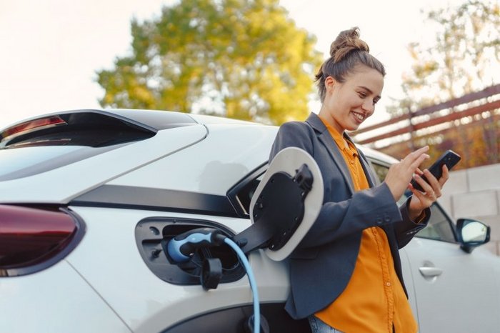 Das Foto zeigt eine junge Frau, die ein E-Auto lädt