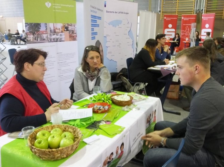 Das Foto zeigt drei Personen im Gespräch am Messestand der CASA-REHA