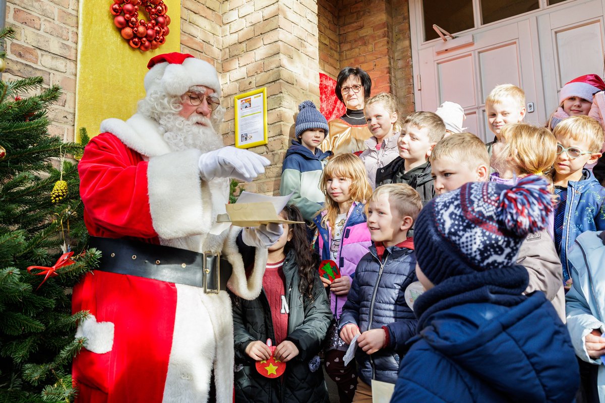 Das Foto zeigt den Weihnachtsmann mit Schulkindern vor dem Eingang in die Weihnachtspostfiliale in Himmelpfort